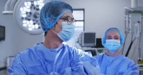 Diverse male and female caucasian surgeons with face masks and protective clothing in hospital