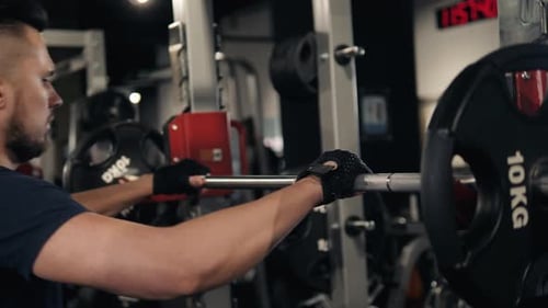 Hands of a Man in Front of the Barbell on the Background of His Back in the Black Pants