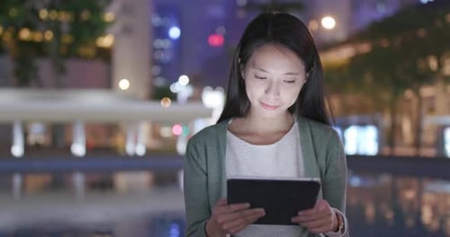 Woman Holding Tablet Computer in City at Night