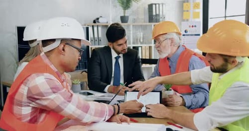 Compañeros de trabajo de construcción y su exitoso ingeniero principal barbudo celebran una reunión conjunta