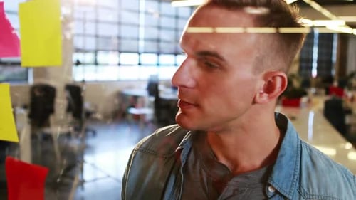 Young Adult Man Writing on Glass Wall in Office
