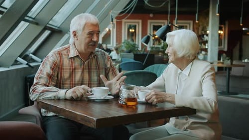 Smiling Man and Woman of Old Age Talking and Drinking Tea in Modern Cafe