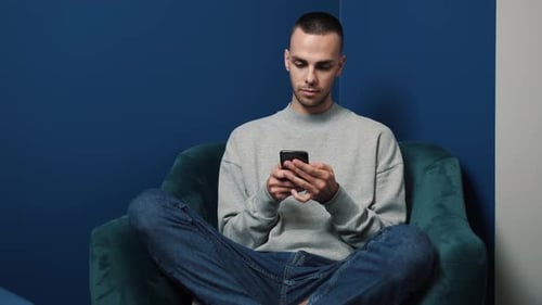 Young Man Using Mobile Phone Sitting in Chair