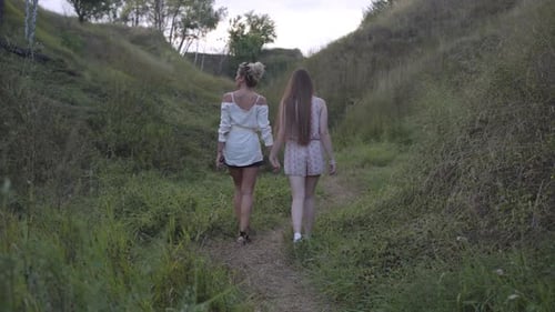 Wide Shot Back View of Two Caucasian Women Walking Outdoors on Overcast Day Holding Hands. Carefree