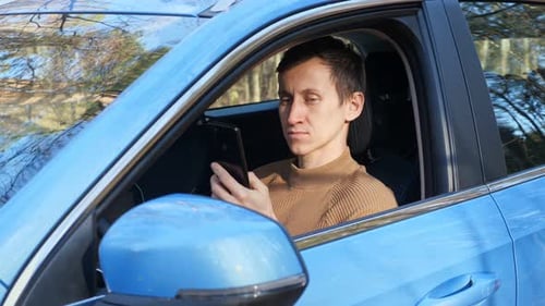 Man Sitting in Car Looking at Smart Phone