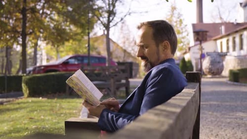 Man Reads Book on Park Bench on Sunny Day