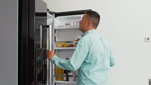 Man Opens Refrigerator and Places Eggs on Shelf
