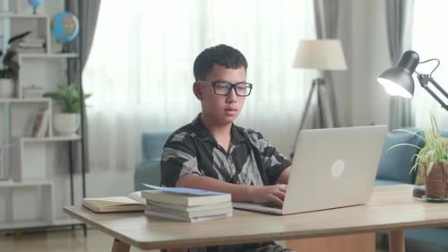 Asia Boy utilise un ordinateur portable à la maison, un adolescent apprend en ligne à partir d'un ordinateur portable