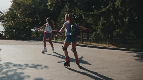 Two Schoolgirls Roller Skating Together in a City Park