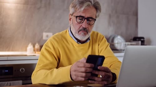 Zeitlupenaufnahme eines reifen Mannes mit Smartphone in der Küche