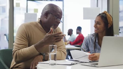 Diverse male and female business colleagues talking and using laptop in office