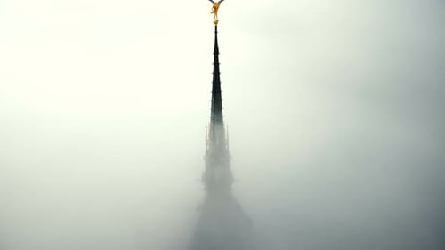 Drone Ascending Above Thick Fog To Reveal Majestic Golden Angel Statue