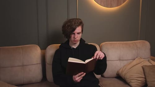 Young Adult Reading Book on Couch Indoors
