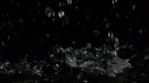 Gießen Sie Wasser auf schwarze Oberfläche vor schwarzem Hintergrund. Zeitlupe.