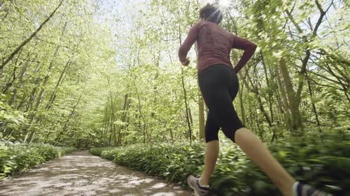 Following Low-Angled Shot of Determined Woman Running Along Path in the Forest