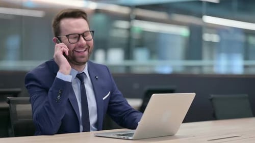 Cheerful Businessman Talking on Phone in Modern Office
