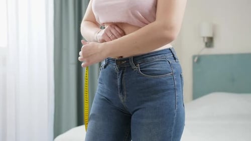 Young Woman Measures Waist in Bedroom