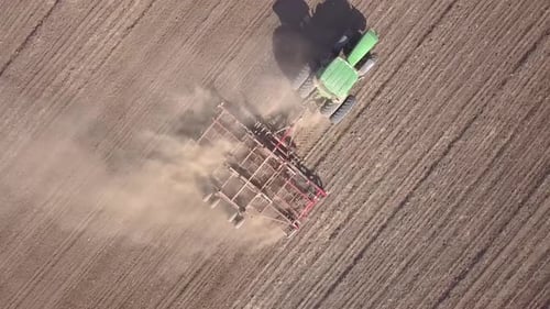 Top down aerial view of green tractor cultivating ground and seeding a dry field. Farmer preparing