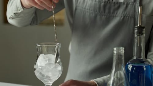 Professional Man Bartender Stirring Ice in the Glass on the Bar Counter