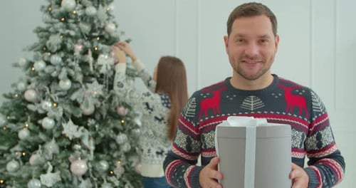 Happy Man Offering Amazing Handmade Holiday Present on Christmas. Beautiful Woman Decorates a
