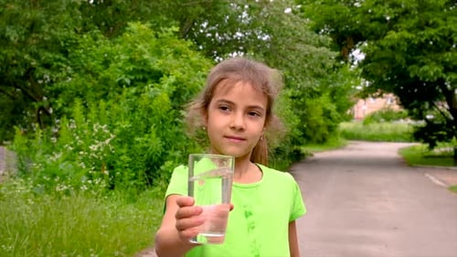 Girl Holds Glass of Water on Tree Lined Road
