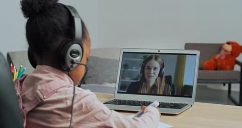View From Behind Afro American Little Girl Child Wears Headphones Looks Into Laptop at Woman Teacher
