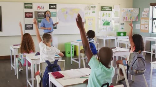 Group of kids raising their hands in the class at school