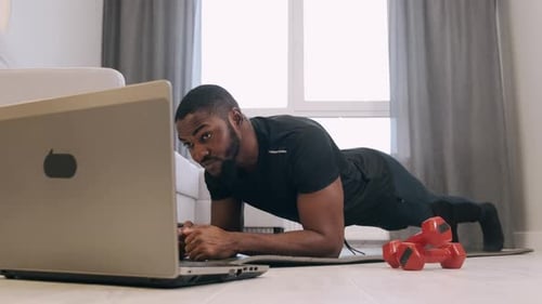 Man Holds Plank Watching Laptop in Living Room