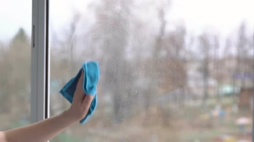 Junge Frau wäscht Fenster mit einem blauen Lappen