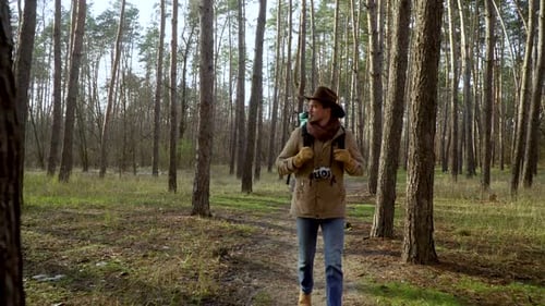 Backpacker with Camera Walks Along a Trail in the Forest