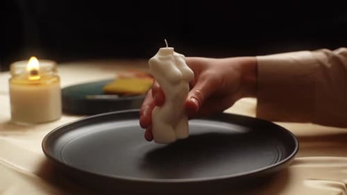 Hand Places Nude Form Candle on Plate