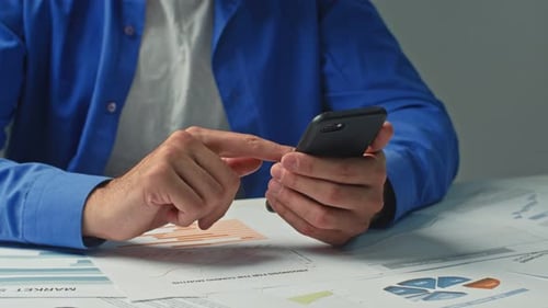 A Business Man's Hands Busy with His Cell Phone at the Office Desk Tracking Business Transactions