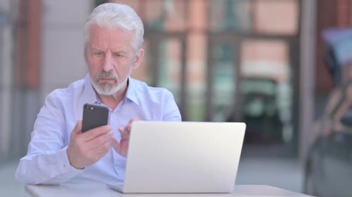 Senior Man Using Smartphone with Laptop Outdoors