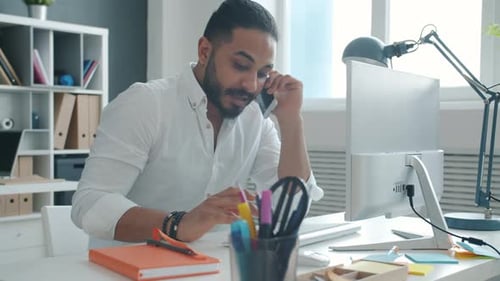 Zeitlupe eines jungen Unternehmers mit gemischter Rasse, der am Handy spricht und mit dem Computer arbeitet