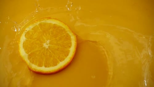 Orange Slice Falling Into Yellow Liquid