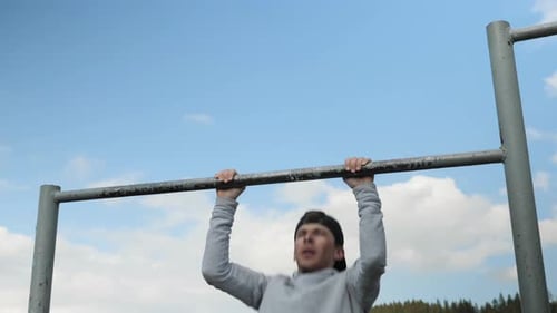 Young athletic male pulls on bar on playground. Street workout