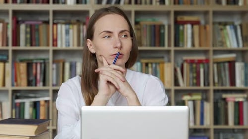 Thoughtful Student Sits in the Library and Thinks About Exams Holding a Pencil in His Hands