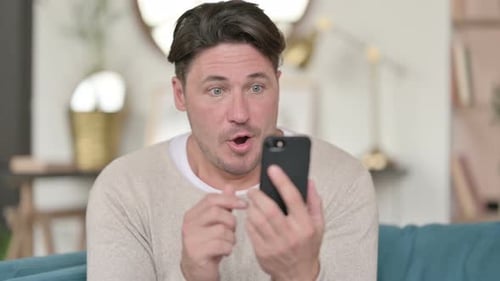 Man Celebrates Success While Using Smartphone at Home