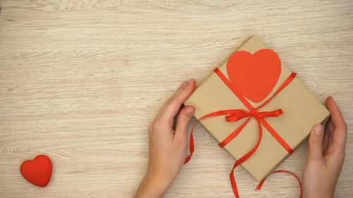 Hands Carefully Placing a Heart-Adorned Gift
