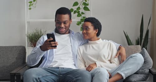 Happy Couple Using Smartphone on Sofa at Home