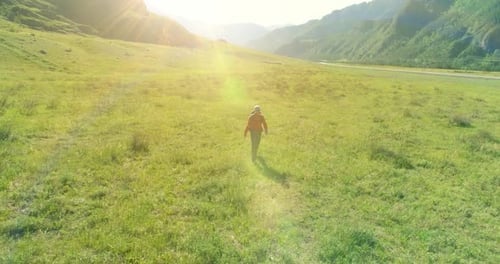 Flight Over Backpack Hiking Tourist Walking Across Green Mountain Field. Huge Rural Valley at Summer