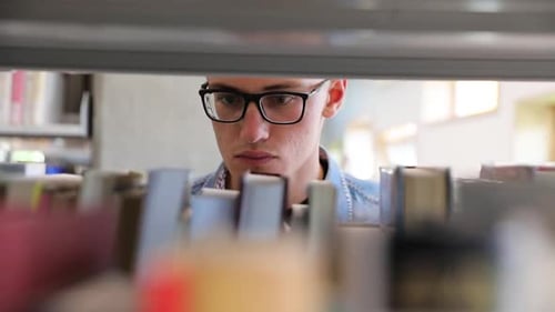 Man Looking For Book On Bookshelves At Library At College