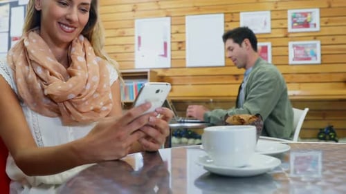 Woman Uses Smartphone, Man Works at Cafe