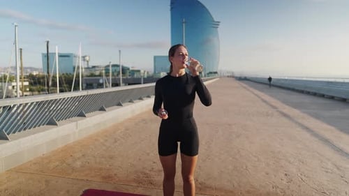 Athletic Woman Drinking Water on Waterfront Walkway