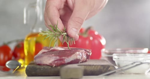 The Men's Hand Puts Rosemary on Raw Beef Ribeye Steak.