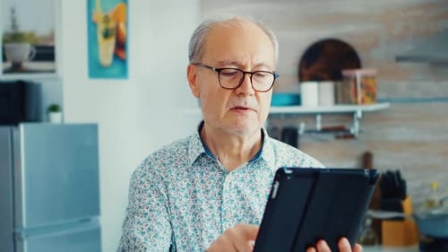 Senior Man Smiling While Using Tablet Indoors