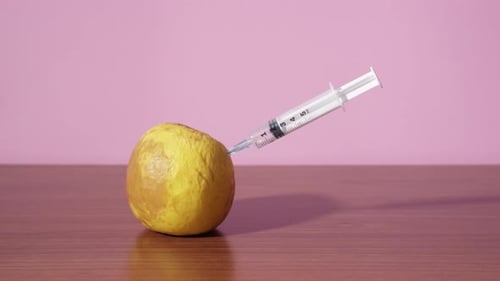 Syringe gives an injection into the rotten green apple