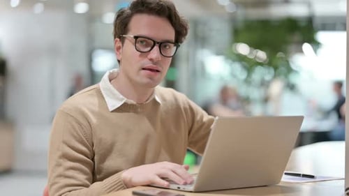 Young Adult Gives Thumbs Up at Laptop in Office