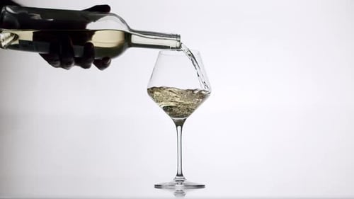 Pouring White Wine into a Glass on White Surface