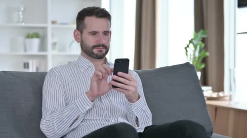 Man Using Smartphone Relaxing on Couch Indoors